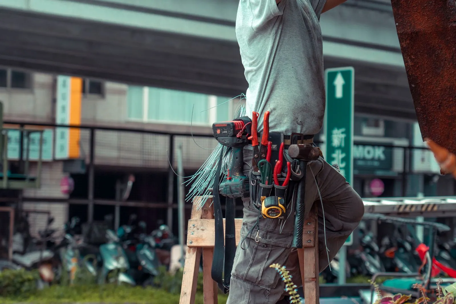 Handyman on a ladder wearing a tool belt, repairing an exterior wall